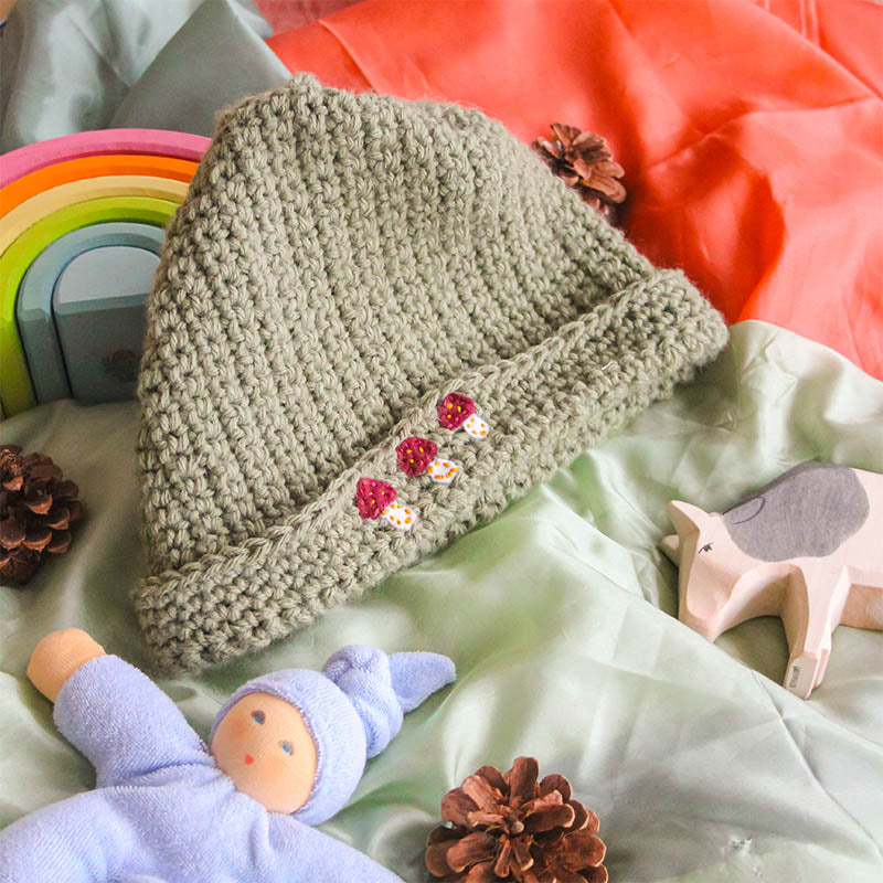 A simple green crochet hat sits next to Waldorf toys and playsilks.