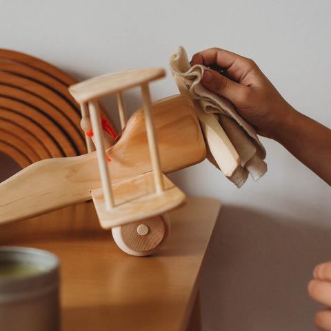 A hand wiping a wooden airplane with a cloth Cleaning and caring for wooden toys 