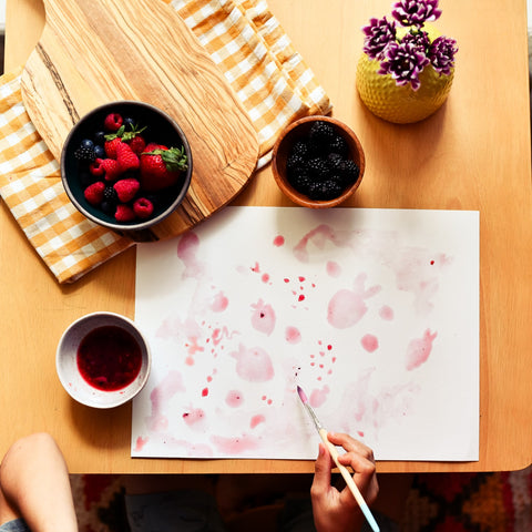 Bowl of berries and white paper with a childs hands painting with ink made from berries