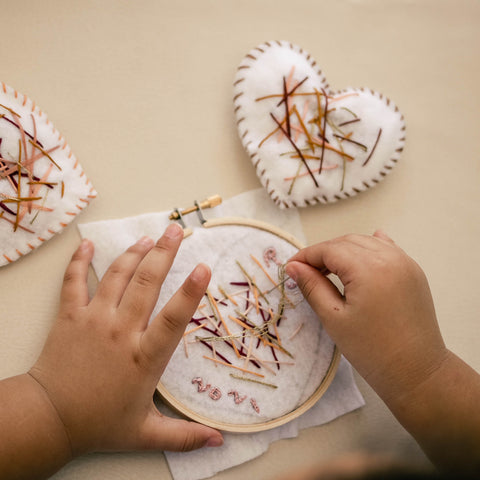 A preschooler doing simple embroidery decorations for a DIY Valentine.