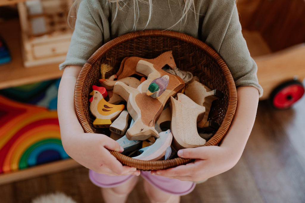 A child's arms hold a basket full of Ostheimer wooden animals from Bella Luna Toys