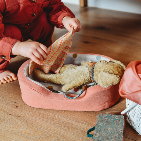 Maileg dog wearing collar and bed, child tucking the dog in under a small blanket