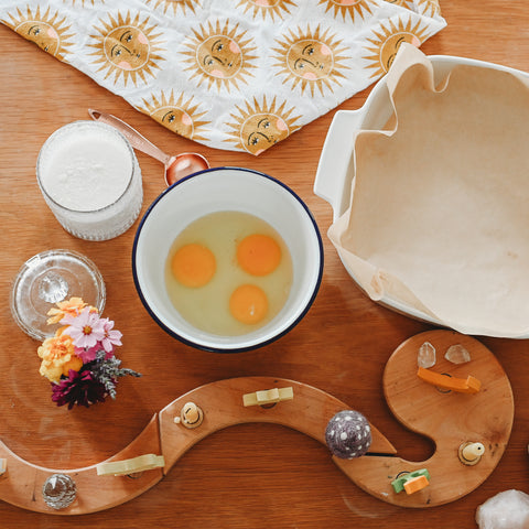 A bowl of 3 cracked eggs next to a corning ware dish lined with parchment paper and a glass jar of sugar