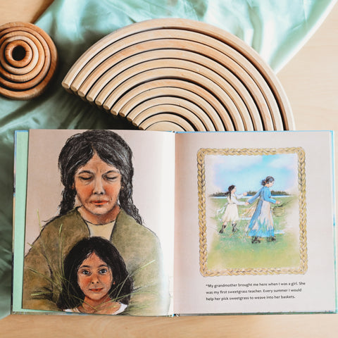 Inside page of the picture book titled The First Blade of Sweetgrass. It lays open on a table resting partway on top of a natural wood colored grimm's rainbow and a green playsilk