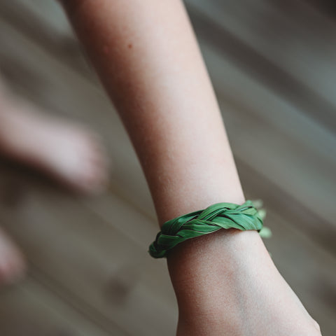 A white child's arm wearing a braided grass bracelet