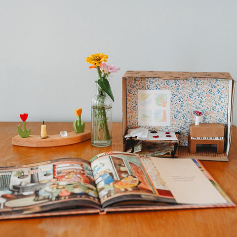 Shoebox diorama of a child's room next to a slender vase and one section of a waldorf birthday ring