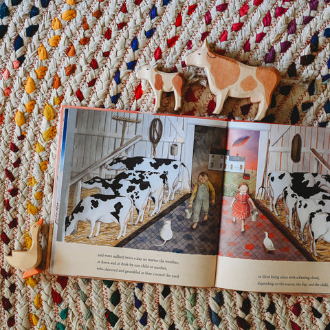 Picture book farmhouse opened to a middle page with illustration of two children carrying buckets into a barn full of cows