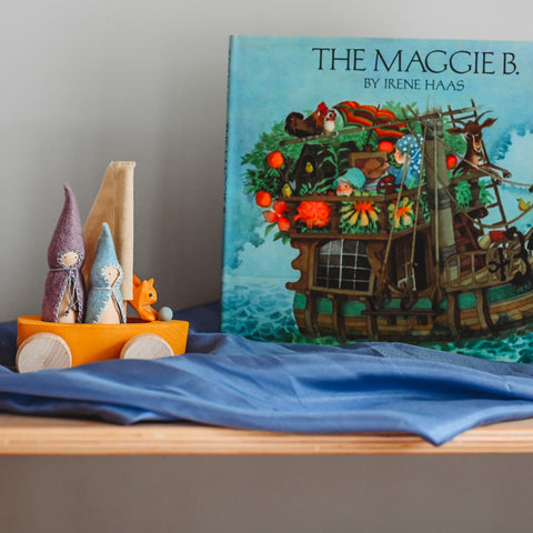 Picture book The Maggie B standing on a shelf behind a blue playsilk with a toy wooden boat on wheels