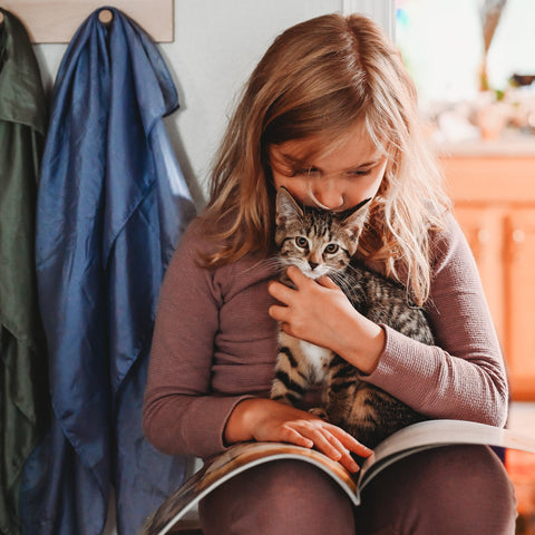 Blonde child reading Miss Maple's Seeds with a small grey kitten in her lap