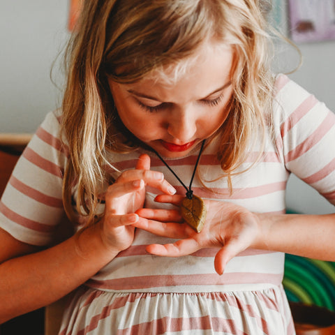 Blonde child holds a soapstone pendant on a necklace in her hand