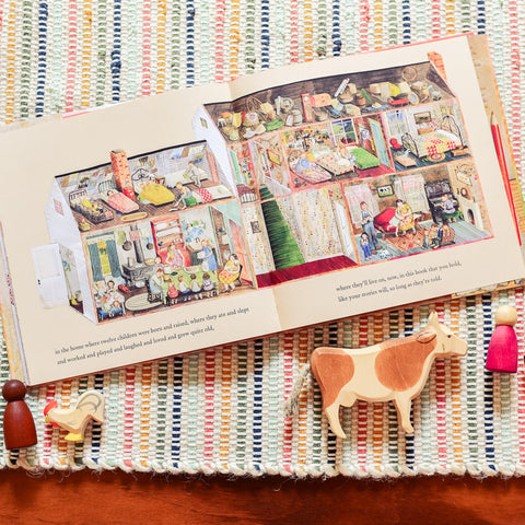 The book Farmhouse opened to a page laying on a striped rug with wooden ostheimer animals and nins laying next to it