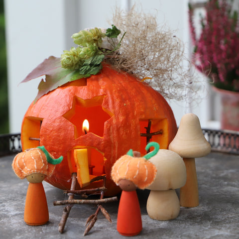 Two wooden peg dolls with pumpkin hats next to a carved pumpkin fairy house waldorf fall tutorial