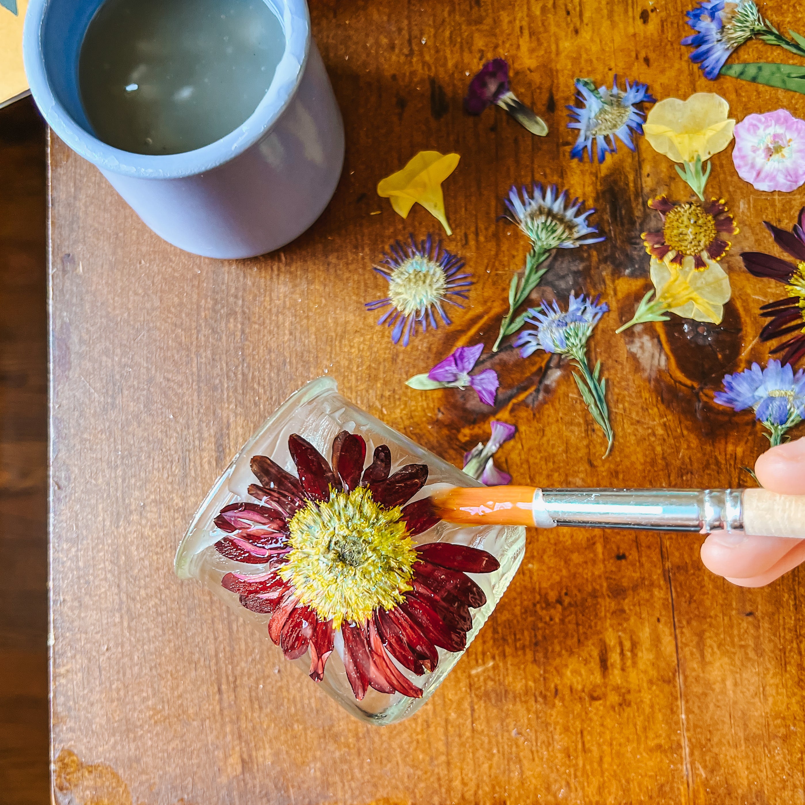 A paint brush gently paints glue over flowers.