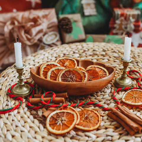 A pile of dried oranges sit in a wooden bowl on a Christmas table.