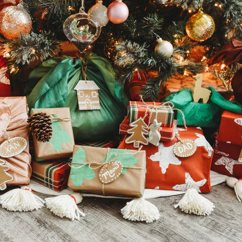 A pile of crafted presents sit under a Christmas tree.