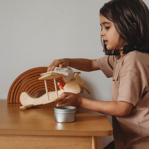 A child using Bee Luna Natural Beeswax Polish to care for wooden toy airplane