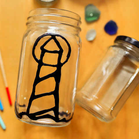 close up of a clear glass jar with the outline of a simple lighthouse drawn in black glue 