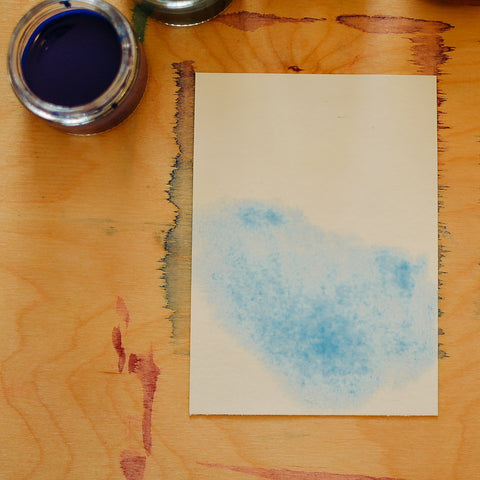 Small piece of watercolor paper with blue paint spread on it