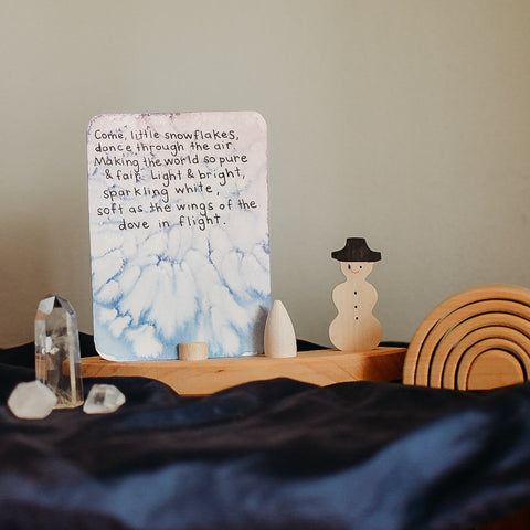 Winter verse on a Waldorf seasonal nature table. It is displayed on a Grimm's birthday ring with the snowman decoration. Next to that sit 3 crystals