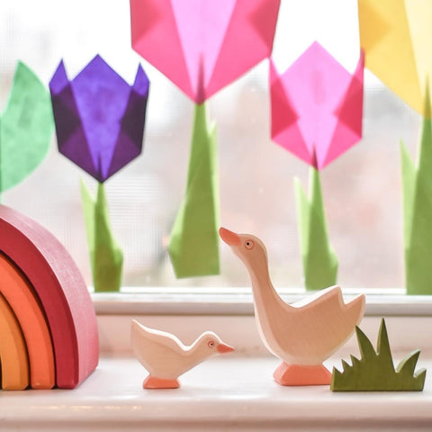 Colorful kite paper flowers decorating a window, on the sill in front of them are a mother and baby Ostheimer wooden goose