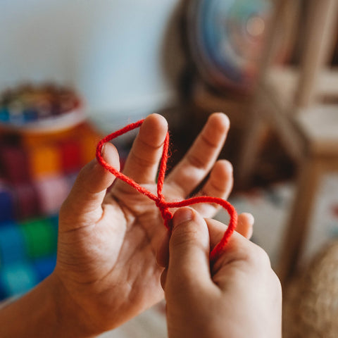 A small child's hand working with red yarn, finger knitting it