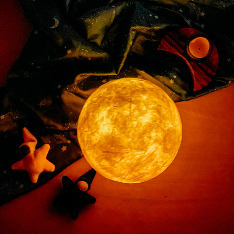 Paper mache sphere shaped lantern made to look like a full moon, in the dark with an led candle inside to make it glow. The texture of the paper mache makes it appear to have craters and other moon like surface features.  