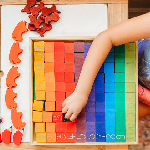 A child plays with colorful blocks marked with numbers. The blocks form a hundred frame