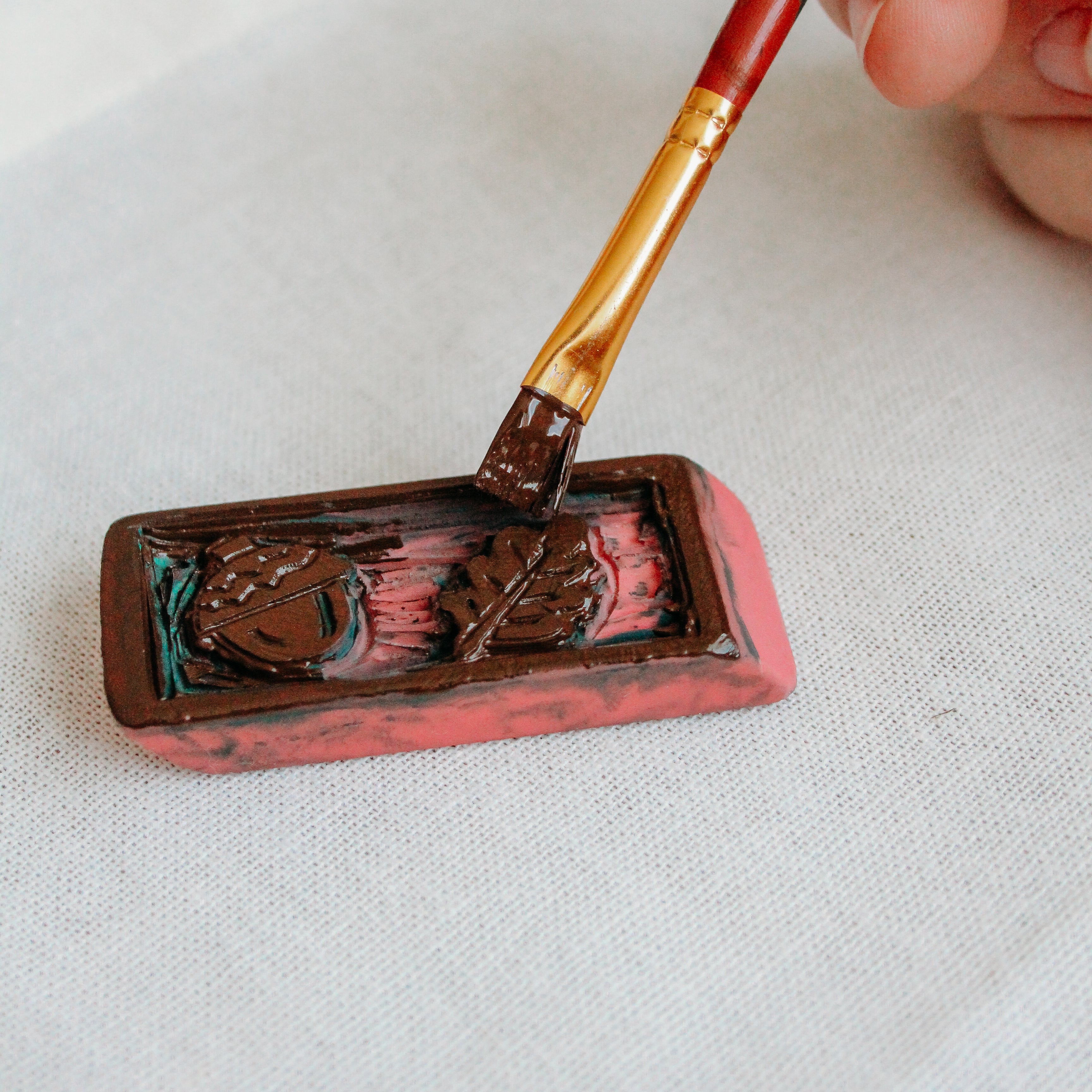 A paintbrush is painting a carved eraser.