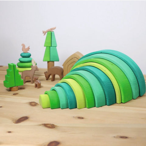 A Grimm's Forest rainbow layed out from smallest to largest with their edges slightly overlapping to create what looks like a hill. There are other toys around this that are made to look like trees and wooden animals