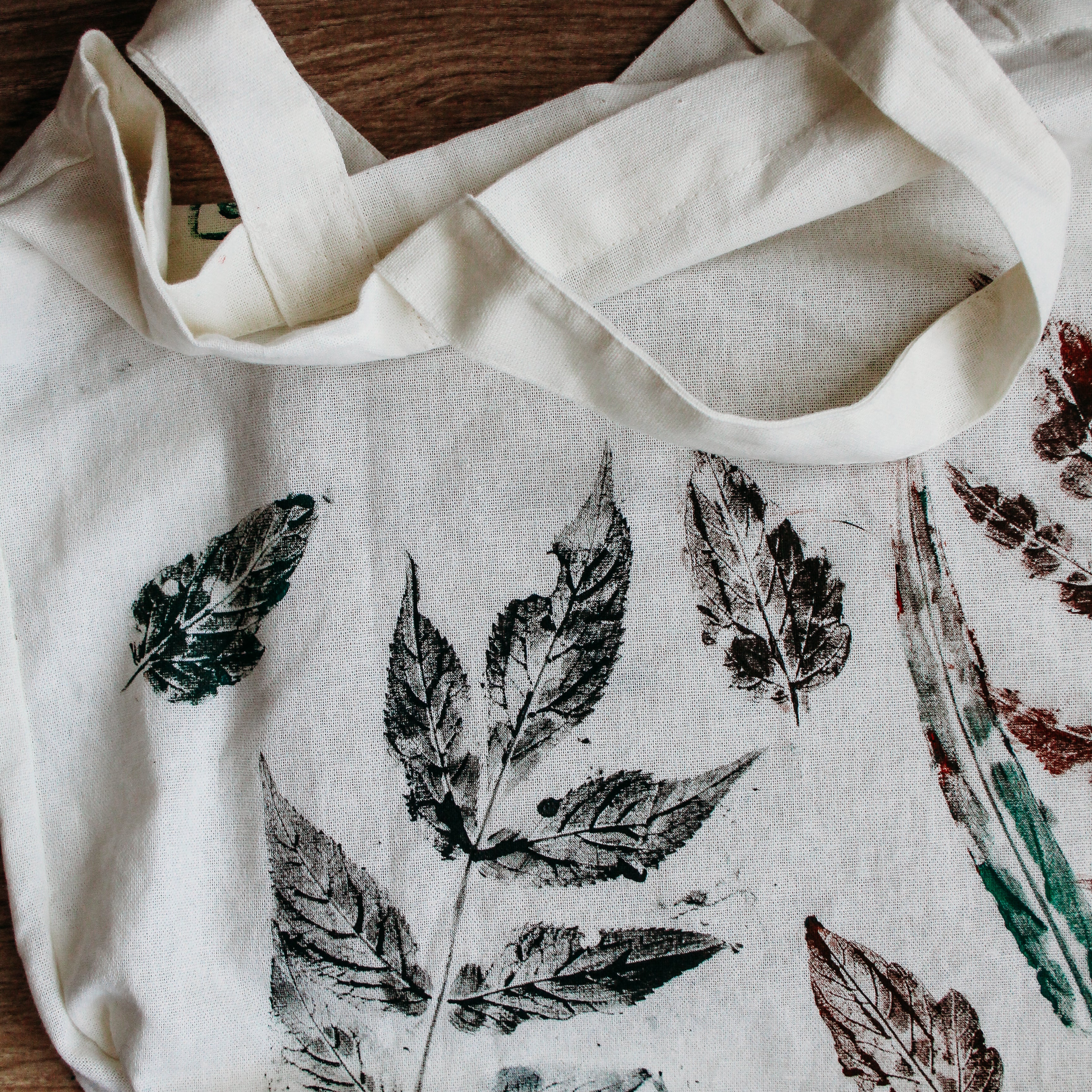A canvas bag sits on a table covered in leaf prints.