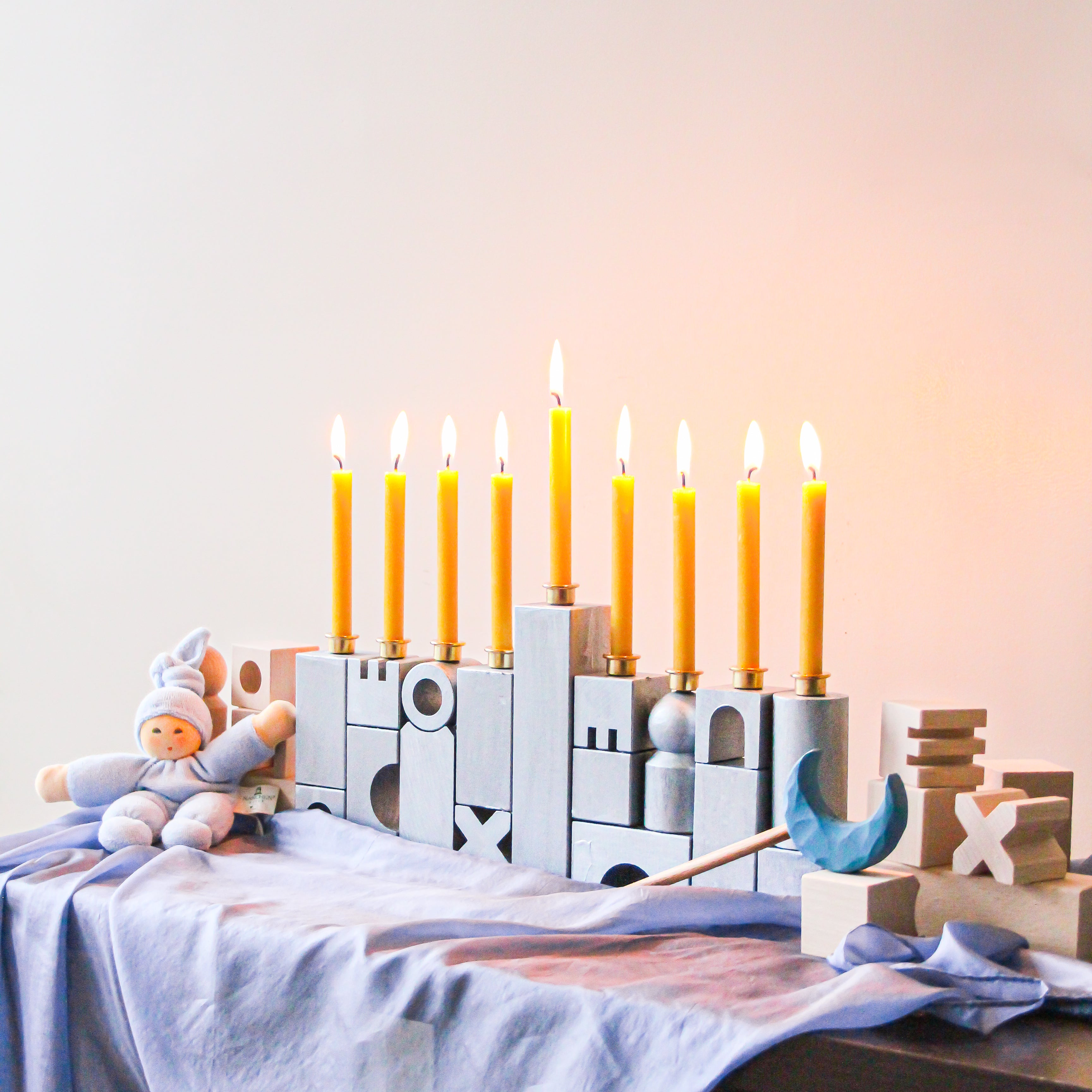 A menorah made of HABA blocks sits on a blue playsilk with lit candles.