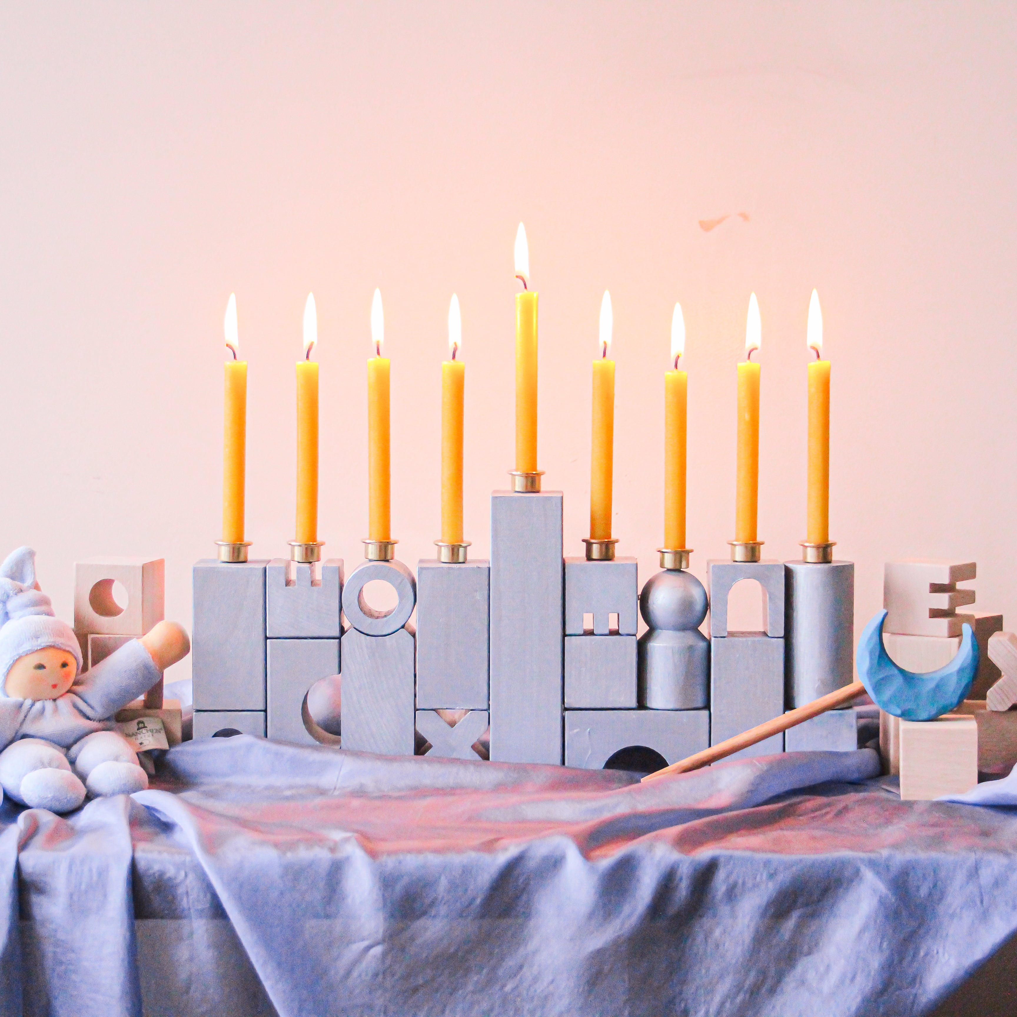 A HABA Block Menorah sits on a playsilk with lit candles.