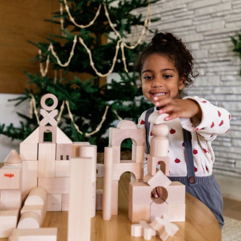 Young girl plays with HABA brand unit building blocks on a table in front of a Christmas tree. 