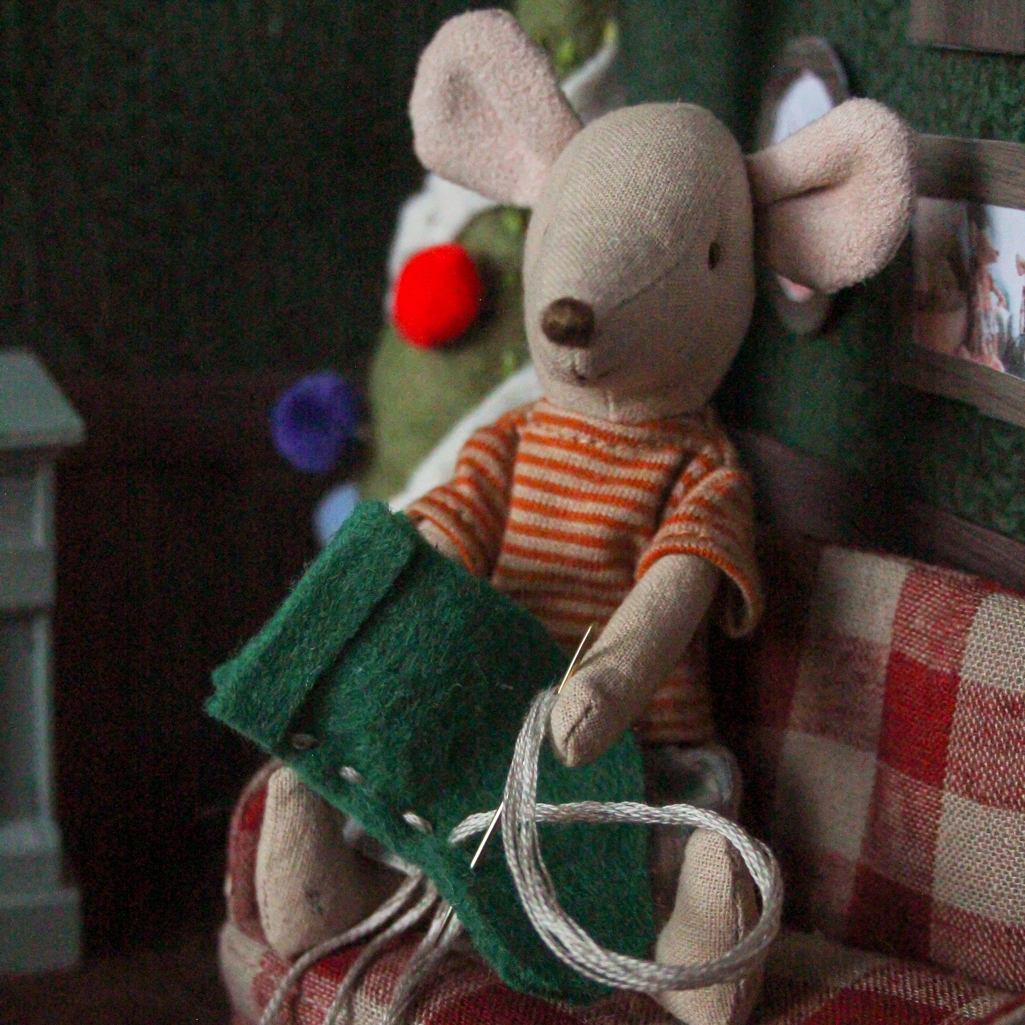 A Maileg Mouse sits embroidering a felt stocking.