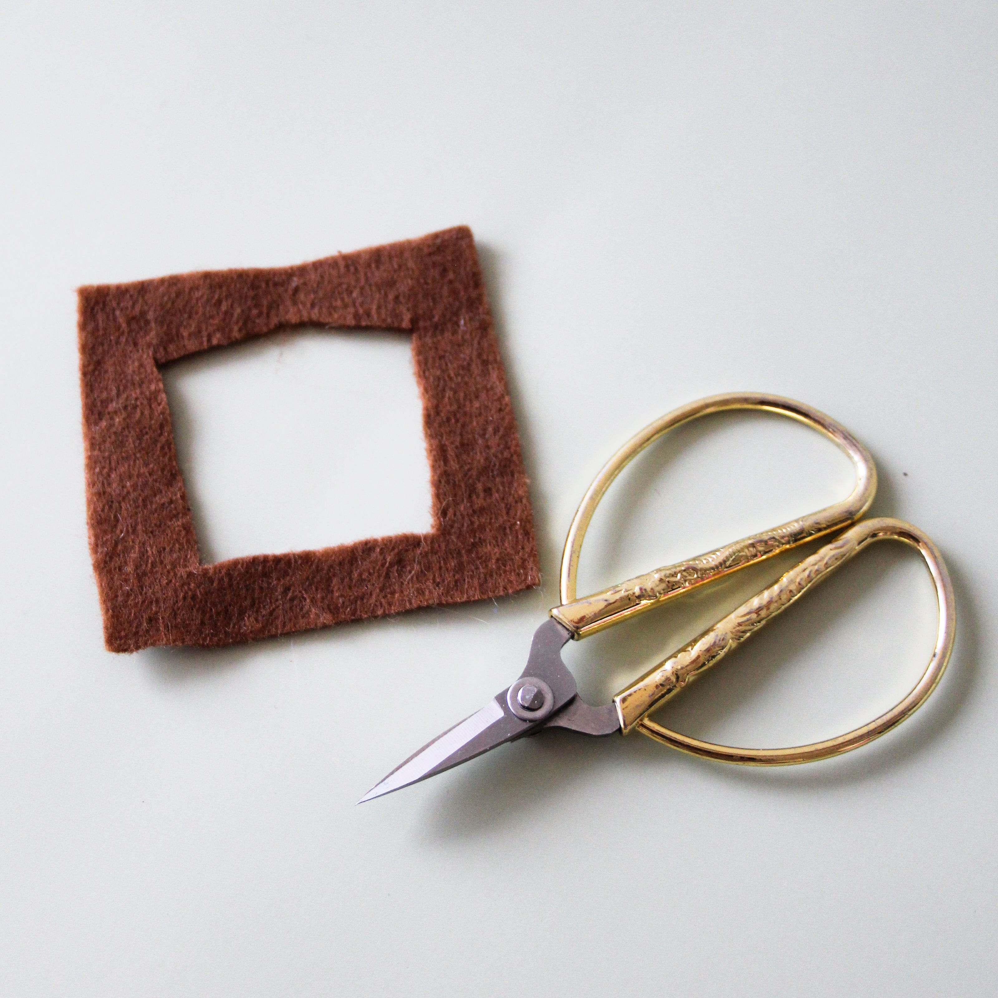 A square is cut from felt on a table.