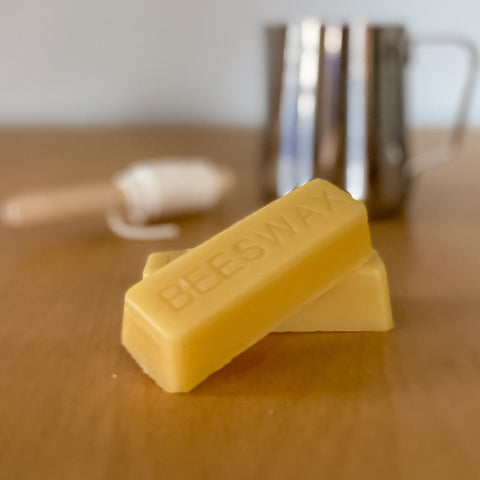 two beeswax blocks in front of cotton candle wick wrapped around clothespin and metal pitcher