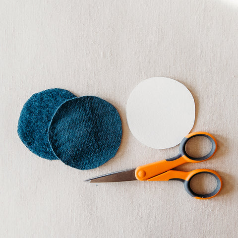 Two circular pieces of merino wool scrap fabric and a circle template with craft scissors