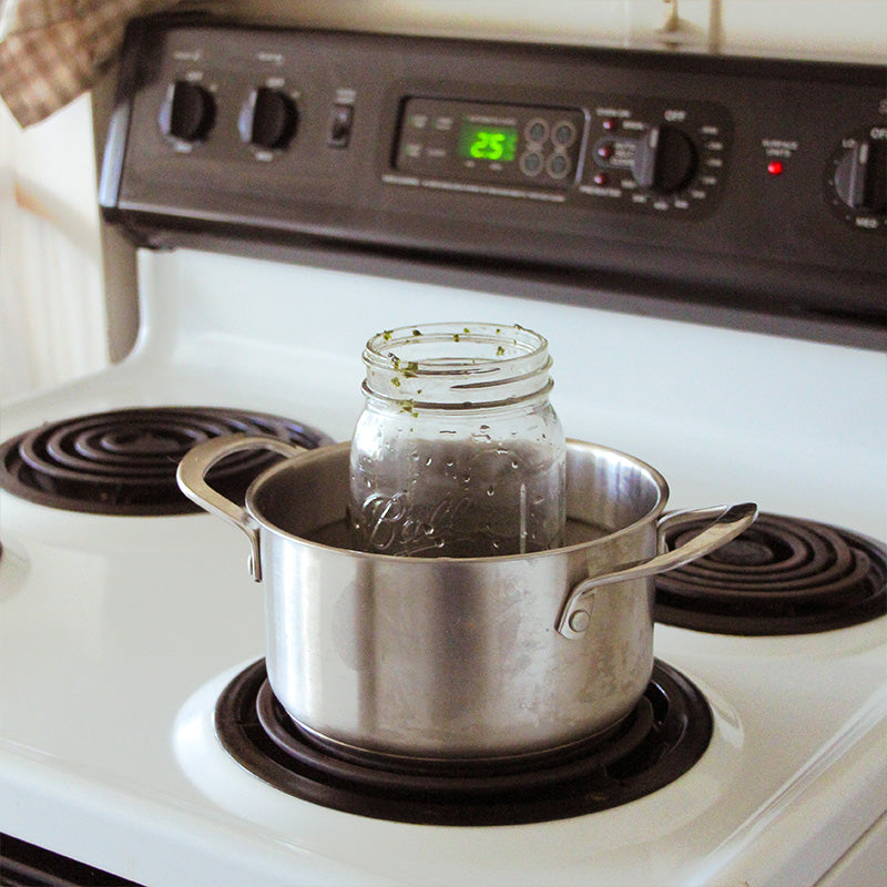 A mason jar sits double boiling on a stove.