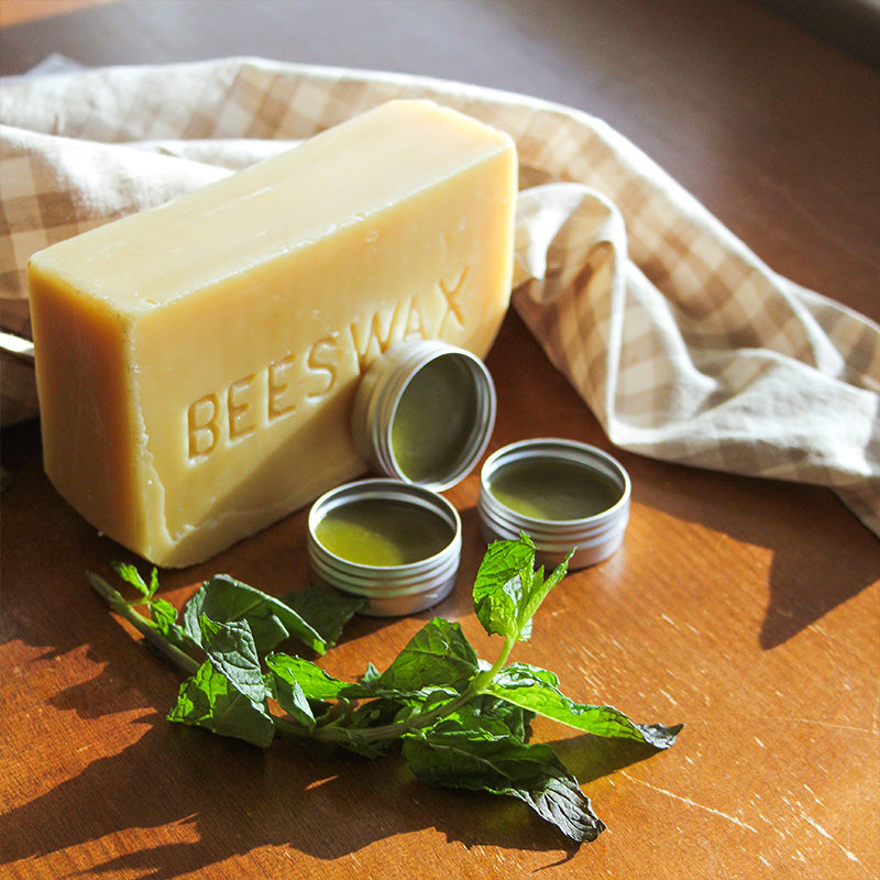 Beeswax lip balm sits with beeswax and mint on a table with a gingham napkin.