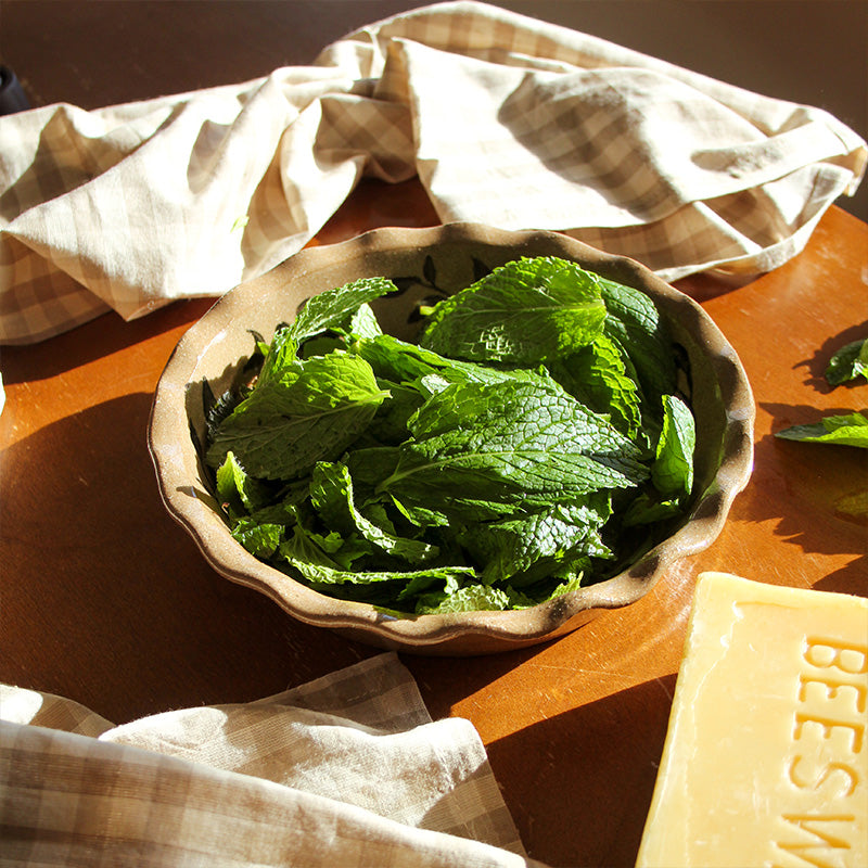 Fresh mint leaves sit in a crafted pie dish with beeswax and gingham napkins.