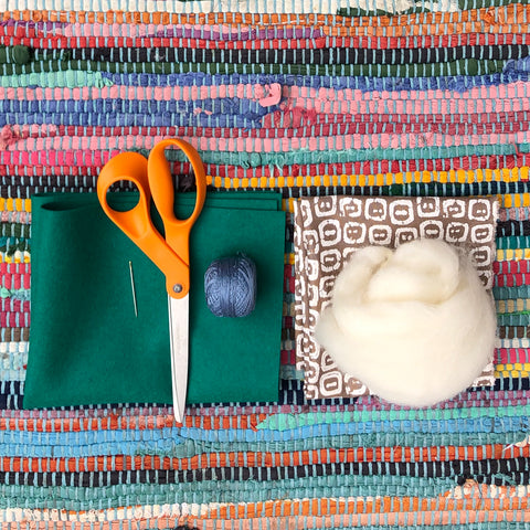 Scissors, fabric, needle, thread and wool laid on a table. 