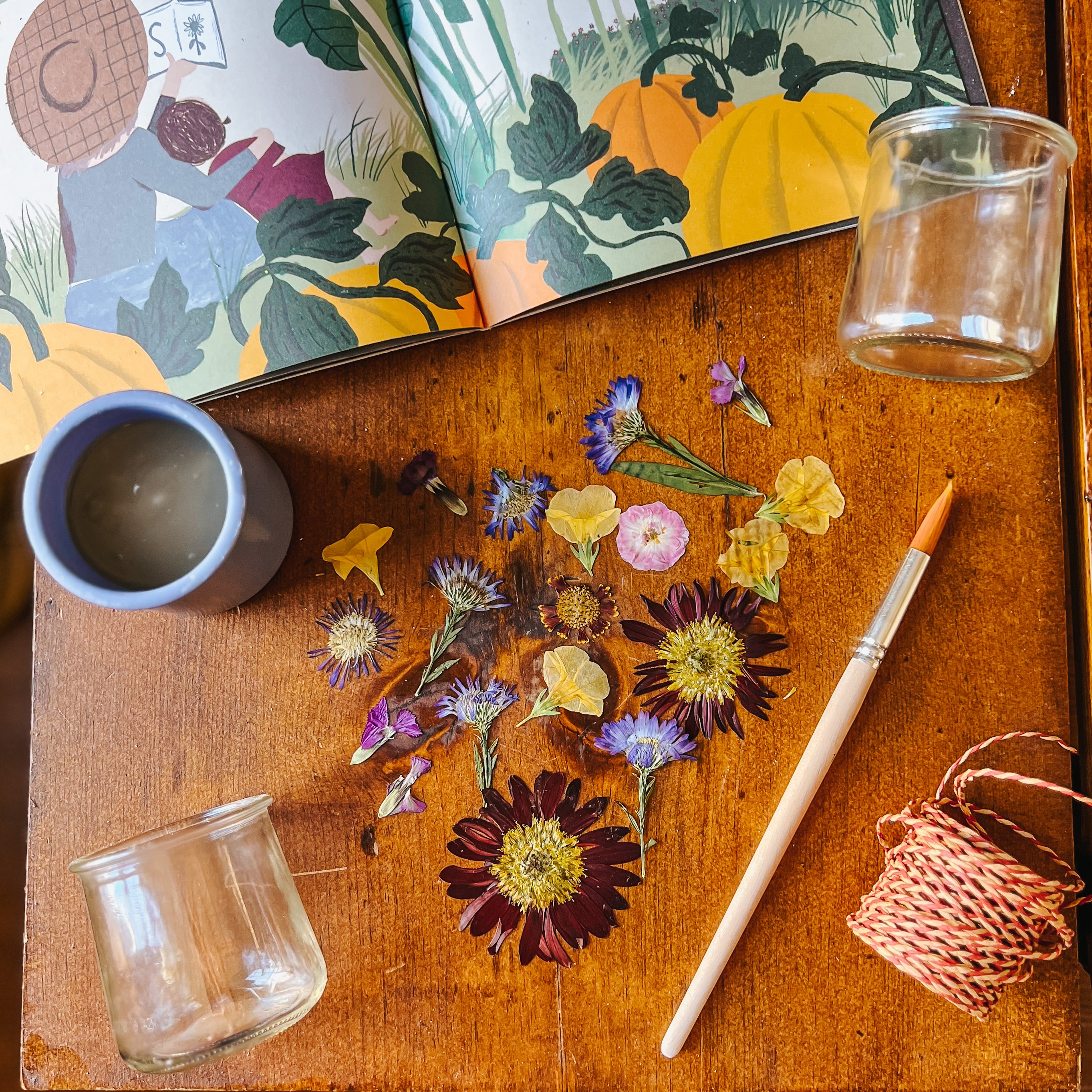 Glass jars and supplies sit on a table with pressed flowers.