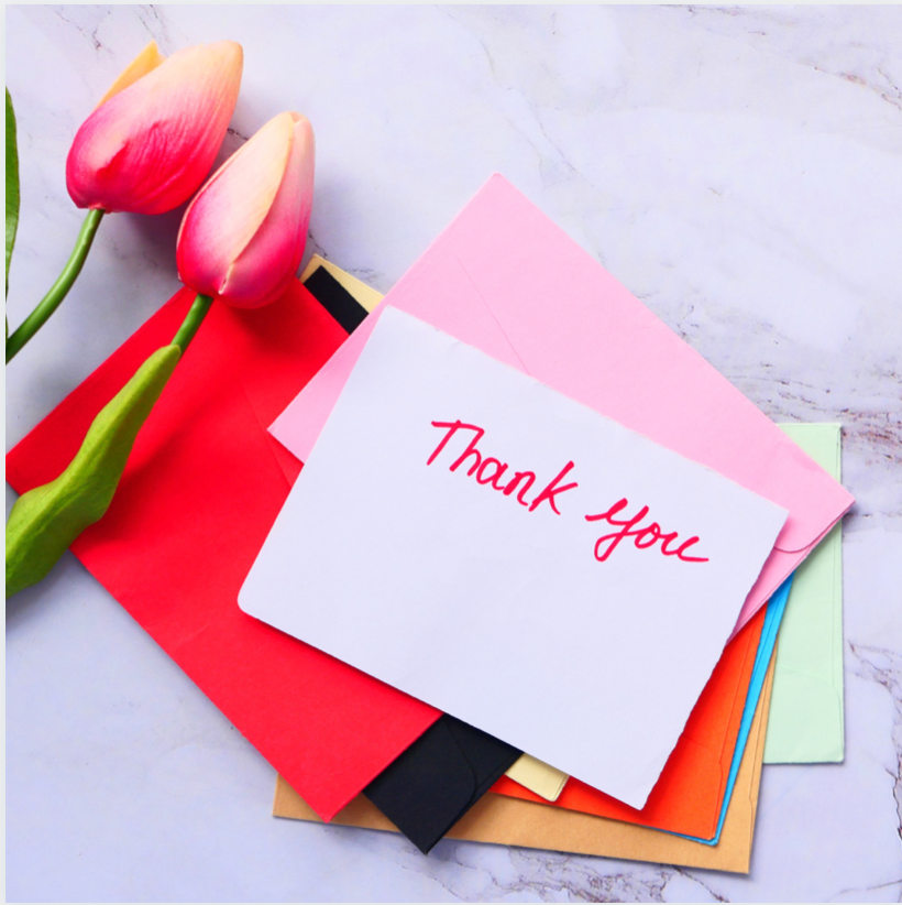 Handwritten thank you cards of many colors and some tulips on a marble table