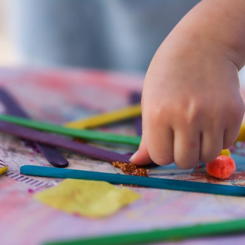 A child's hand gluing pieces to a collage.