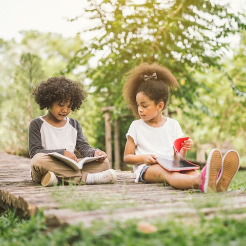 Two children reading books outside.