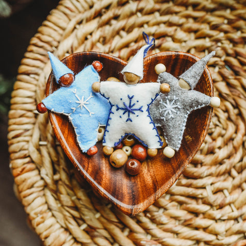 A wooden bowl containing wooden beads and 3 completed felt Waldorf Snowflake Children crafted dolls.