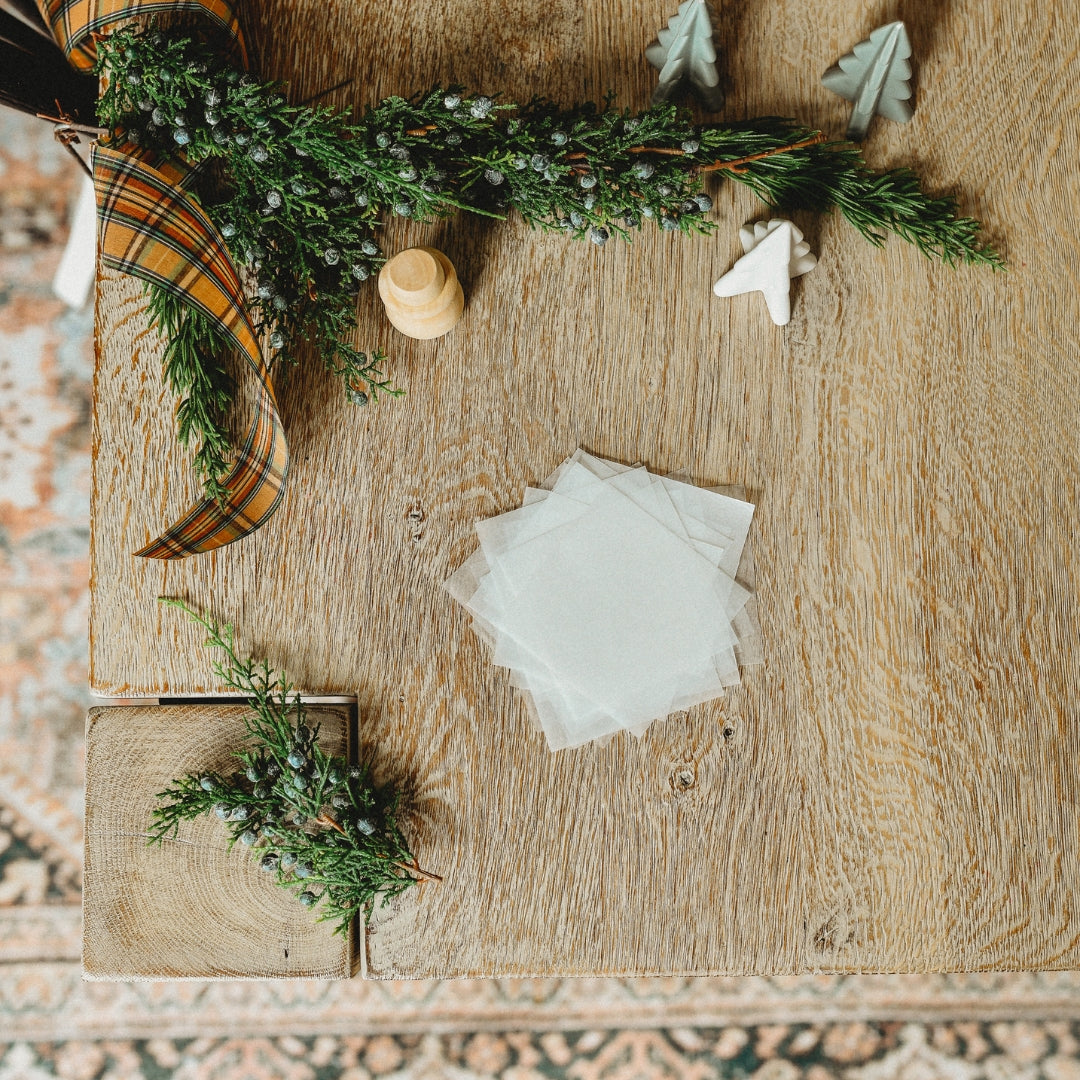 Unfolded kite paper sits on a table surrounded by pine.