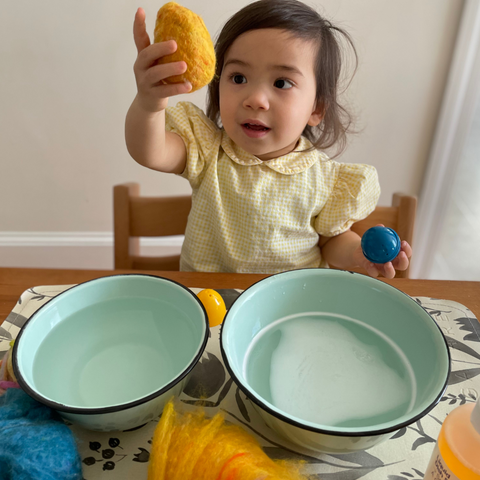 young child holding wet felted egg shape in front of two large bowls of water and balls of wool roving