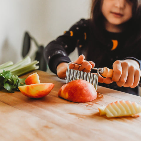 A child with dark hair cutting an apple with a crinkle cutter