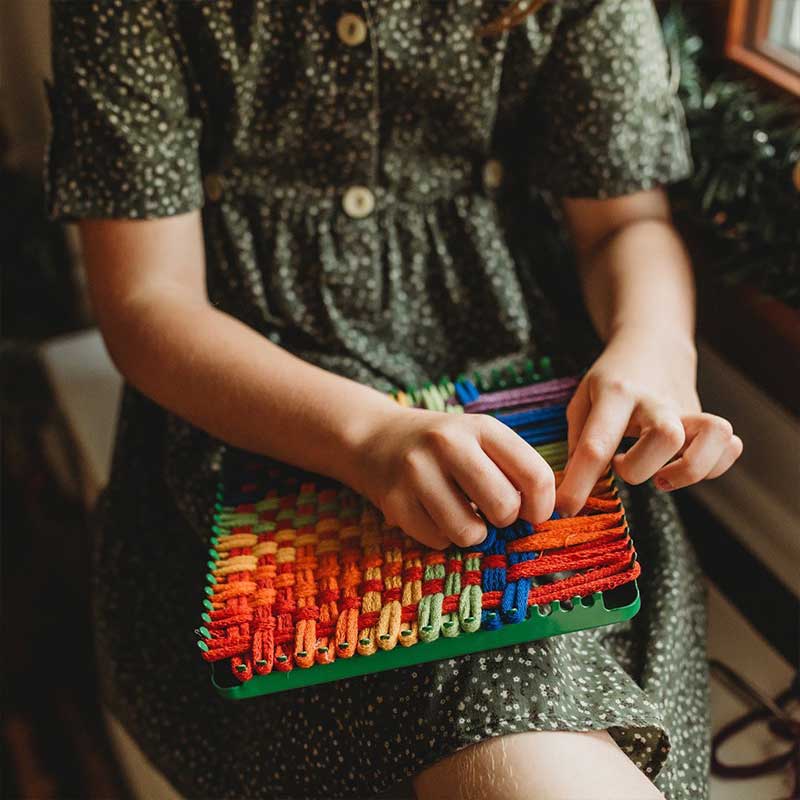 A young girl is using a loom.